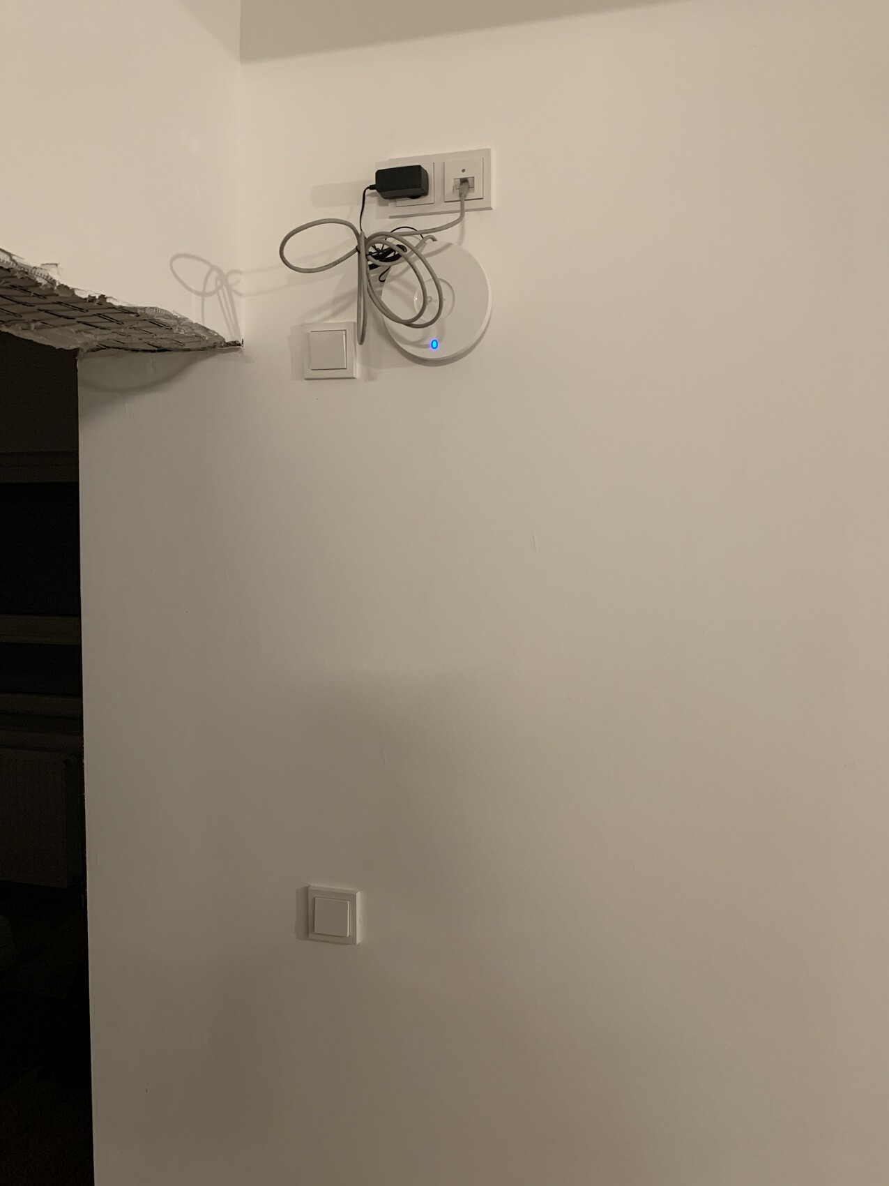 Weiße Wand mit rundem WLAN-Access-Point (blaues Licht) und losen Kabeln.