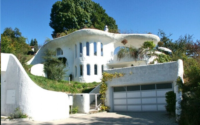 Außenansicht eines weißen organisch geformten Hauses mit Garage und umlaufender Terrasse.