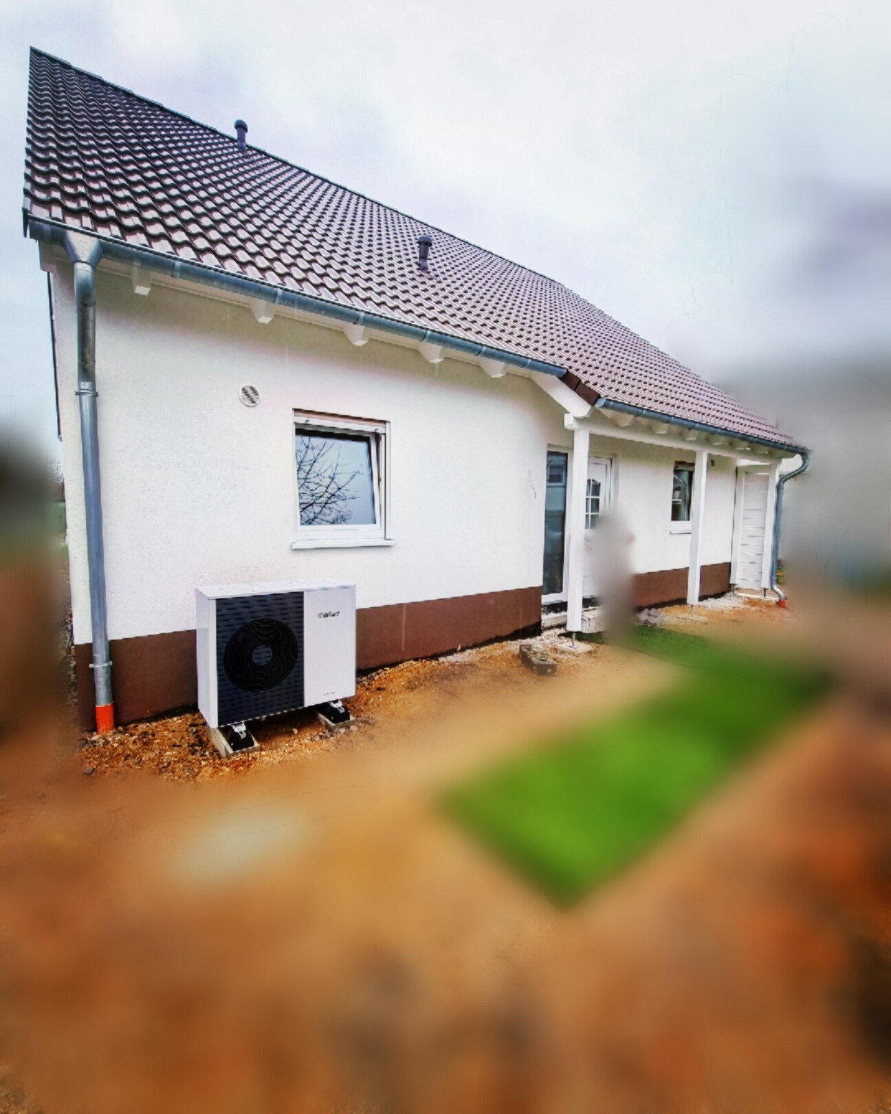Kleines Einfamilienhaus von außen, rotes Ziegeldach, weiße Fassade, Außenkühlgerät vor dem Haus