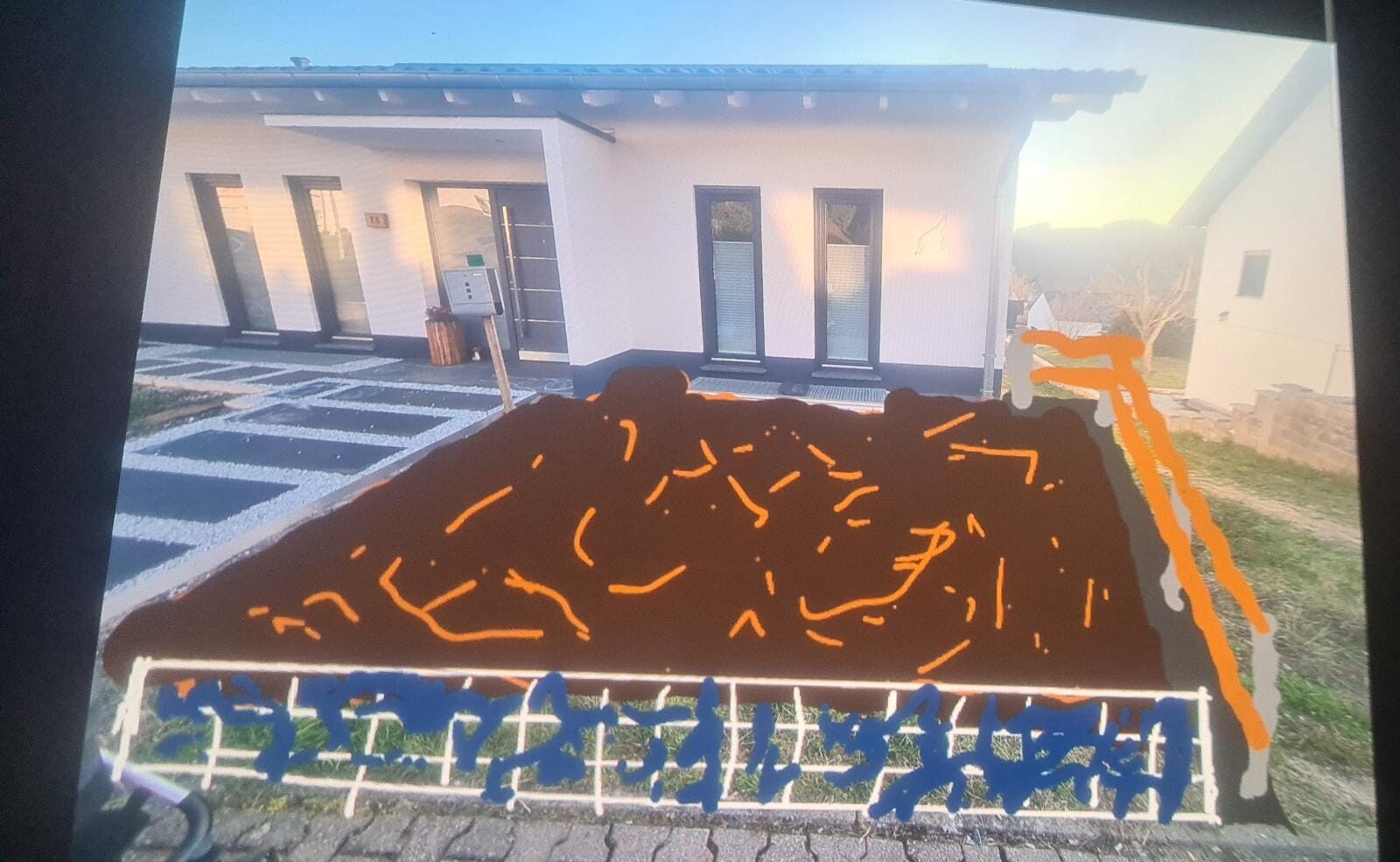 Weißes Einfamilienhaus, davor ein großer dunkler Erd-/Materialhaufen mit orange Markierungen.