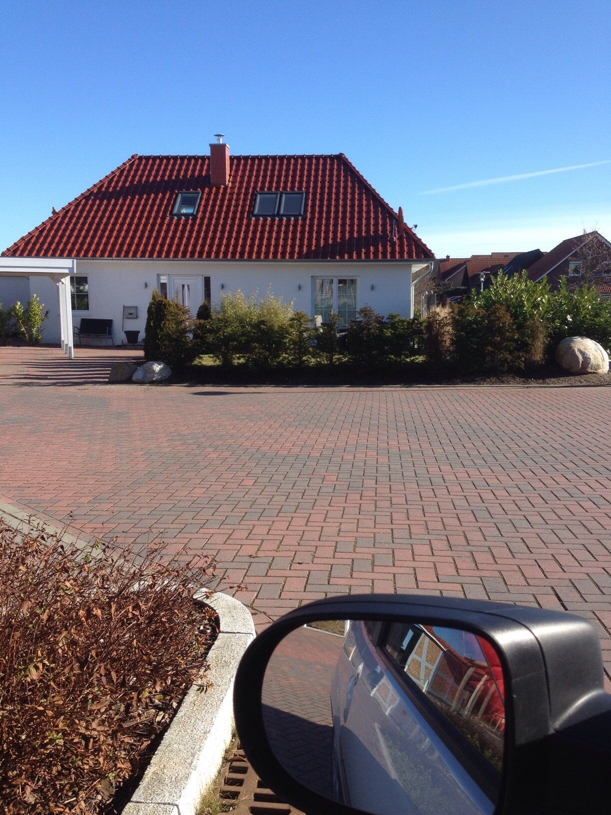 Weißes Einfamilienhaus mit rotem Dach, Vorgarten und Autospiegel im Vordergrund