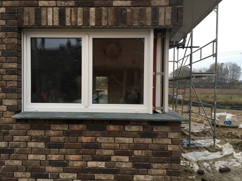 Fenster in einer Ziegelwand mit Baugerüst rechts, Baustelle mit Abdeckungen und Erde dahinter.