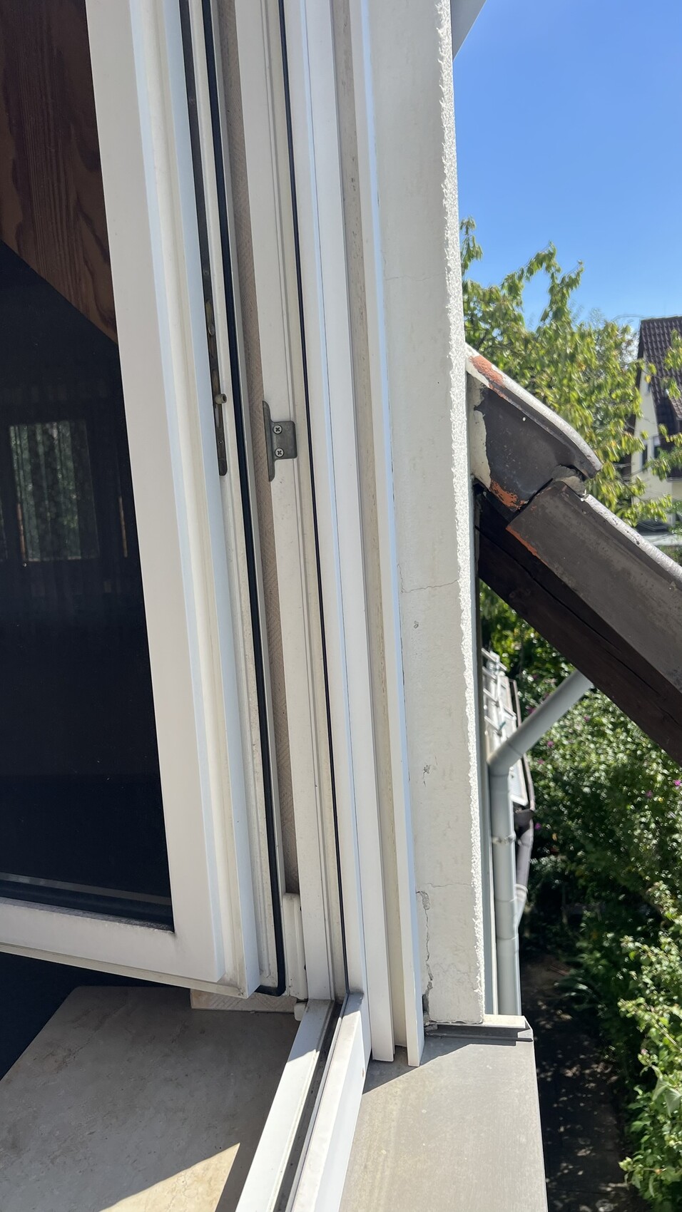 Außenansicht eines weißen Fensterrahmens mit geöffnetem Fenster und Dachziegeln am Gebäude