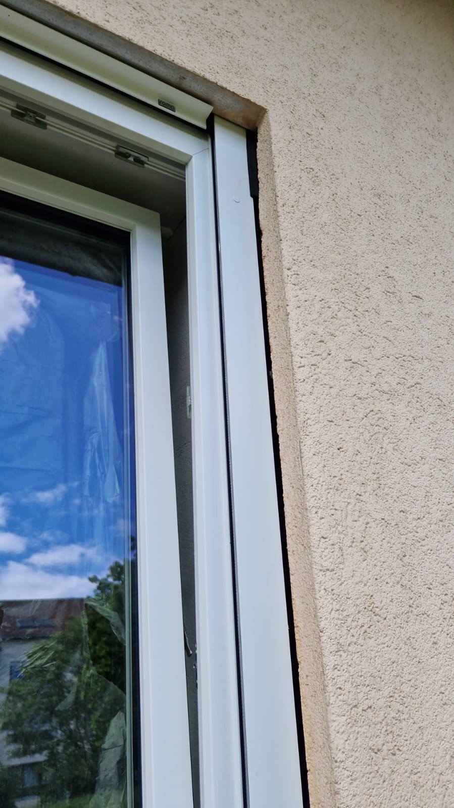 Weißer Fensterrahmen vor beige verputzter Wand; Spiegelbild von Himmel und Bäumen.