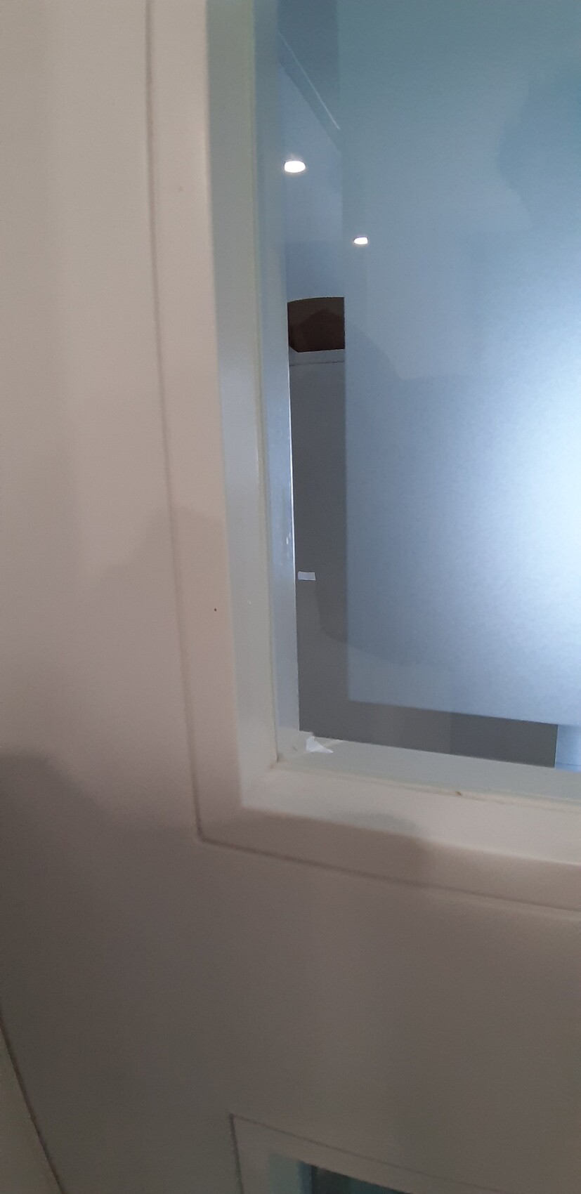 Weißer Fensterrahmen mit blau getöntem Glas; unscharfer Innenraum sichtbar.