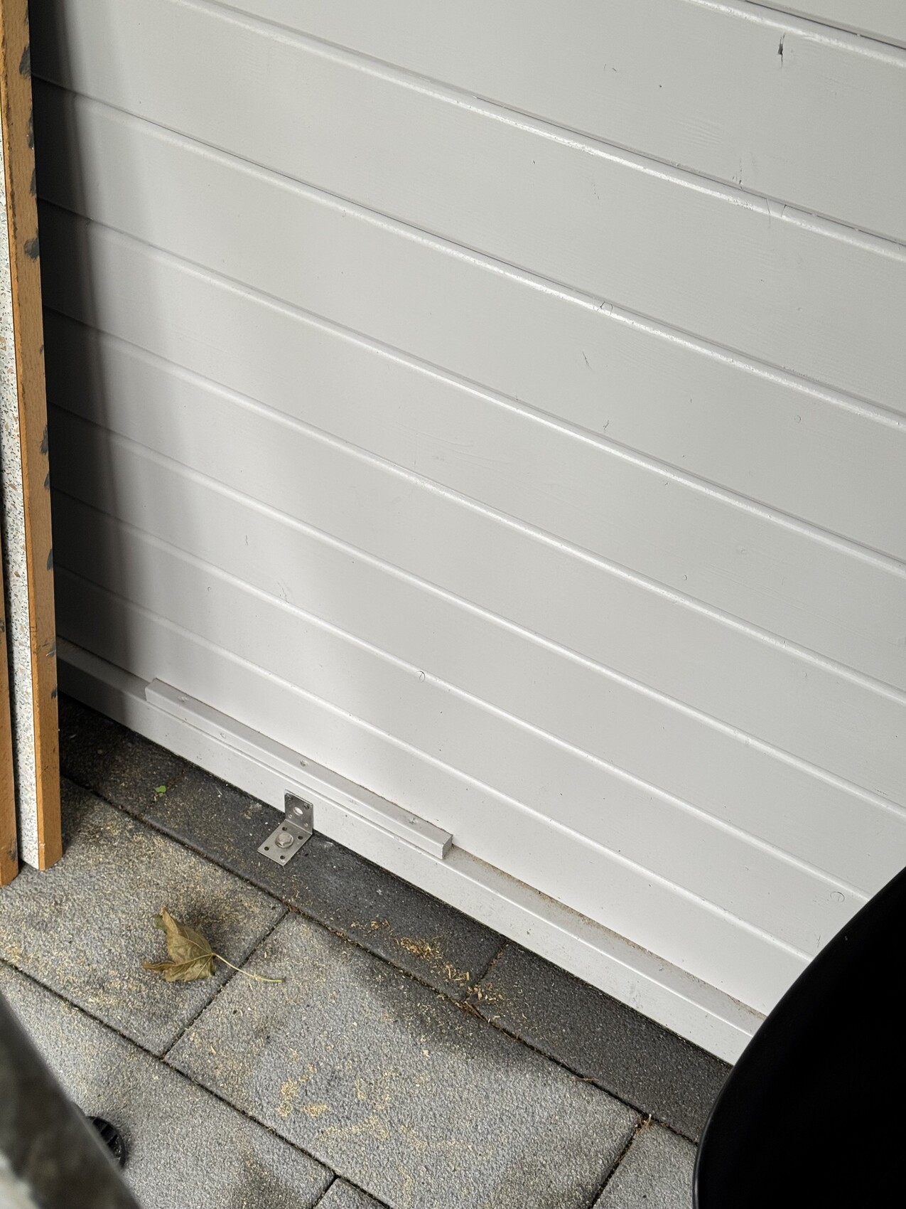 Weiße Garagenwand aus Paneelen mit Bodenschutzblech und Pflasterboden im Vordergrund