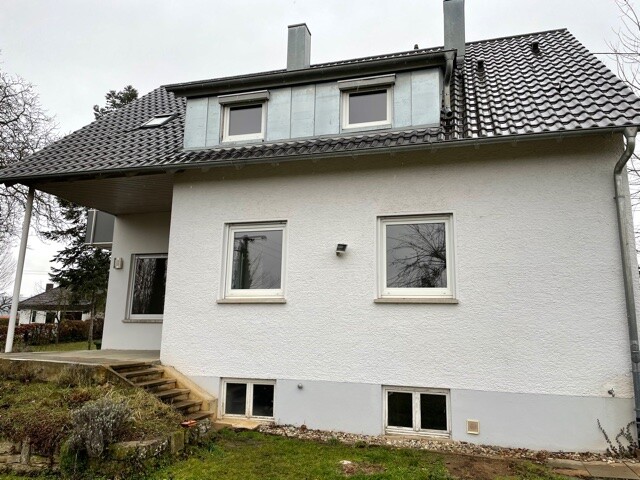 Zweistöckiges helles Haus mit Dachgauben, Eingangstreppe und Garten.