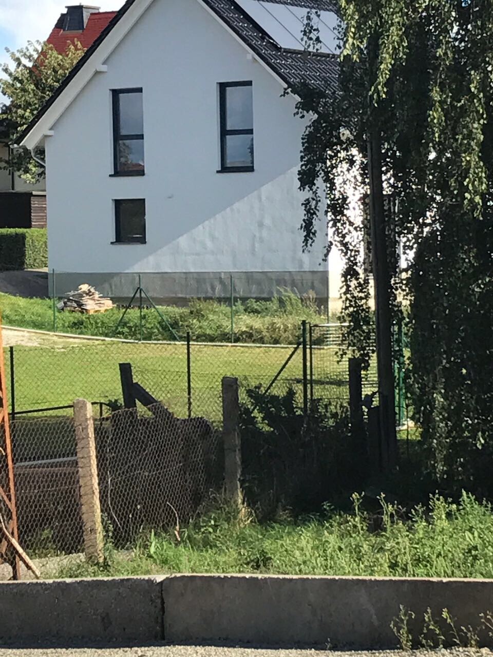Weiße Hausfassade mit grauer Sockel, dunklen Fenstern und Gartenzaun im Vordergrund