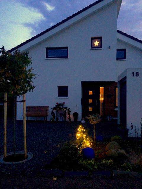 Weißes Haus mit Eingang, Stern im Fenster und ein weihnachtlich beleuchteter Garten.