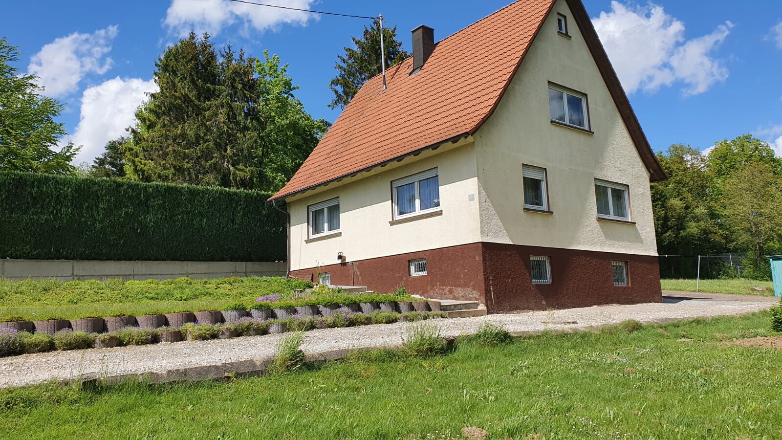 Einfamilienhaus mit rotem Ziegeldach, heller Fassade und Garten im Vordergrund