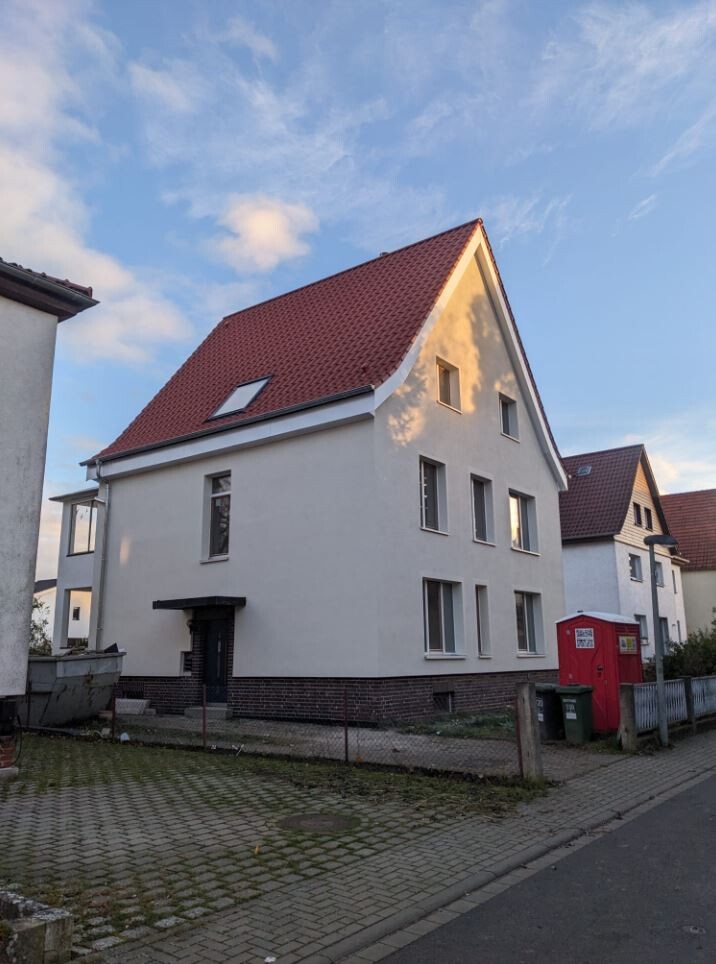 Weiße dreistöckige Wohnhausfront mit rotem Ziegeldach, mehreren Fenstern und Straßenumgebung