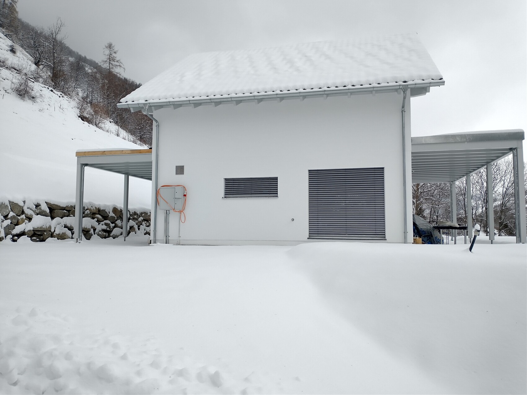 Weißes Einfamilienhaus im Schnee mit seitlichem Carport und verschneiter Umgebung.