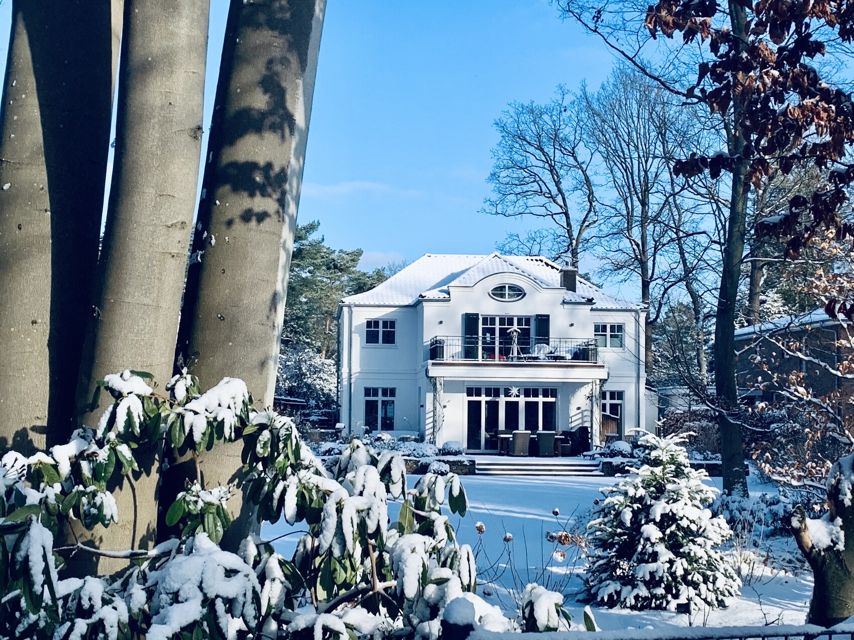 Weiße zweistöckige Villa mit Balkon im verschneiten Garten, blauer Himmel