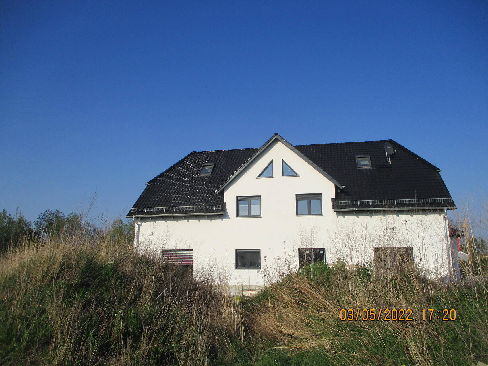 Weißes Haus mit schwarzem Satteldach, Dachgiebel mit Dreiecksfenstern, grasiger Vorgarten