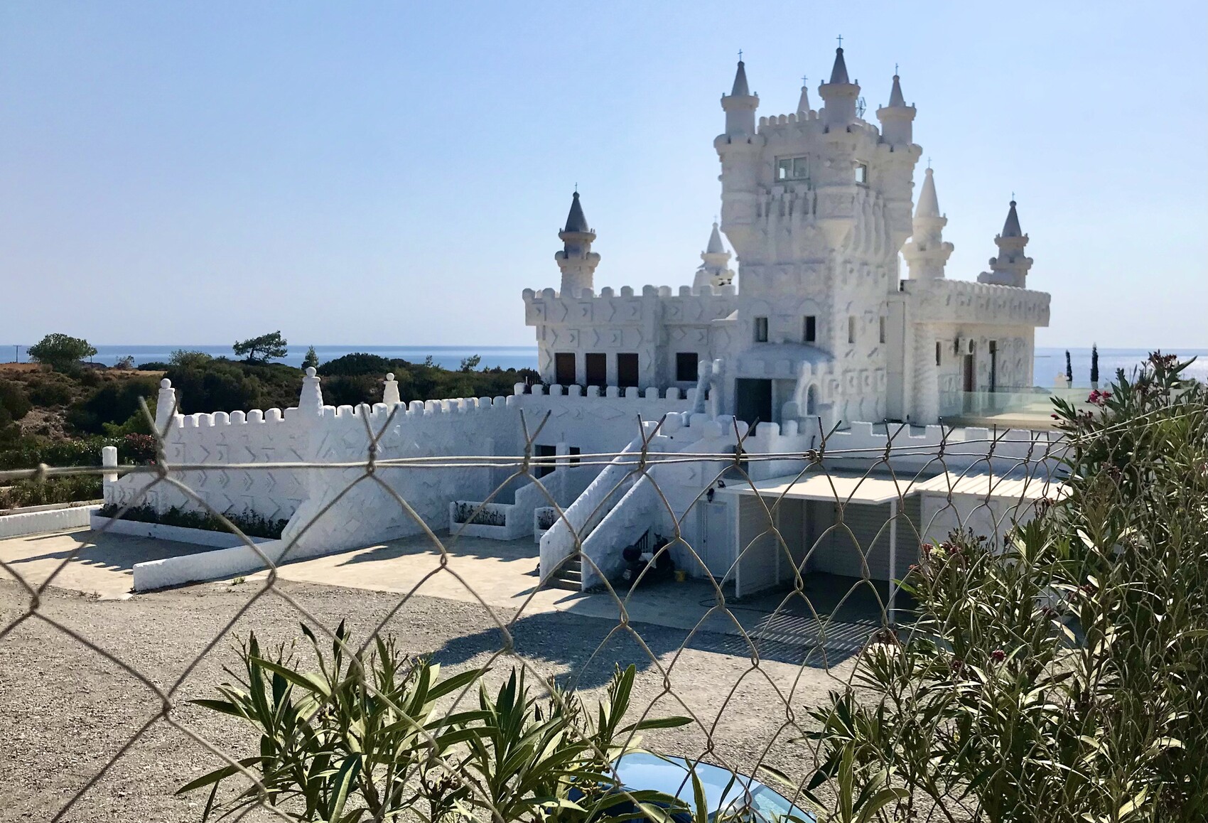 Weisses maerchen-schloss-artiges gebaeude am meer mit turmspitzen hinter zaun