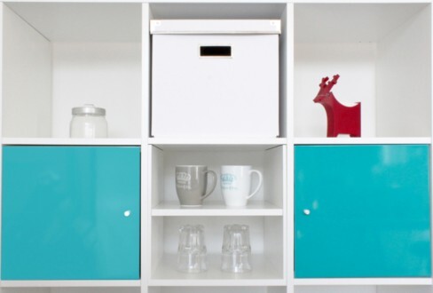 Weißes modulares Regal mit türkis-blauen Türen und Geschirr auf den Fächern
