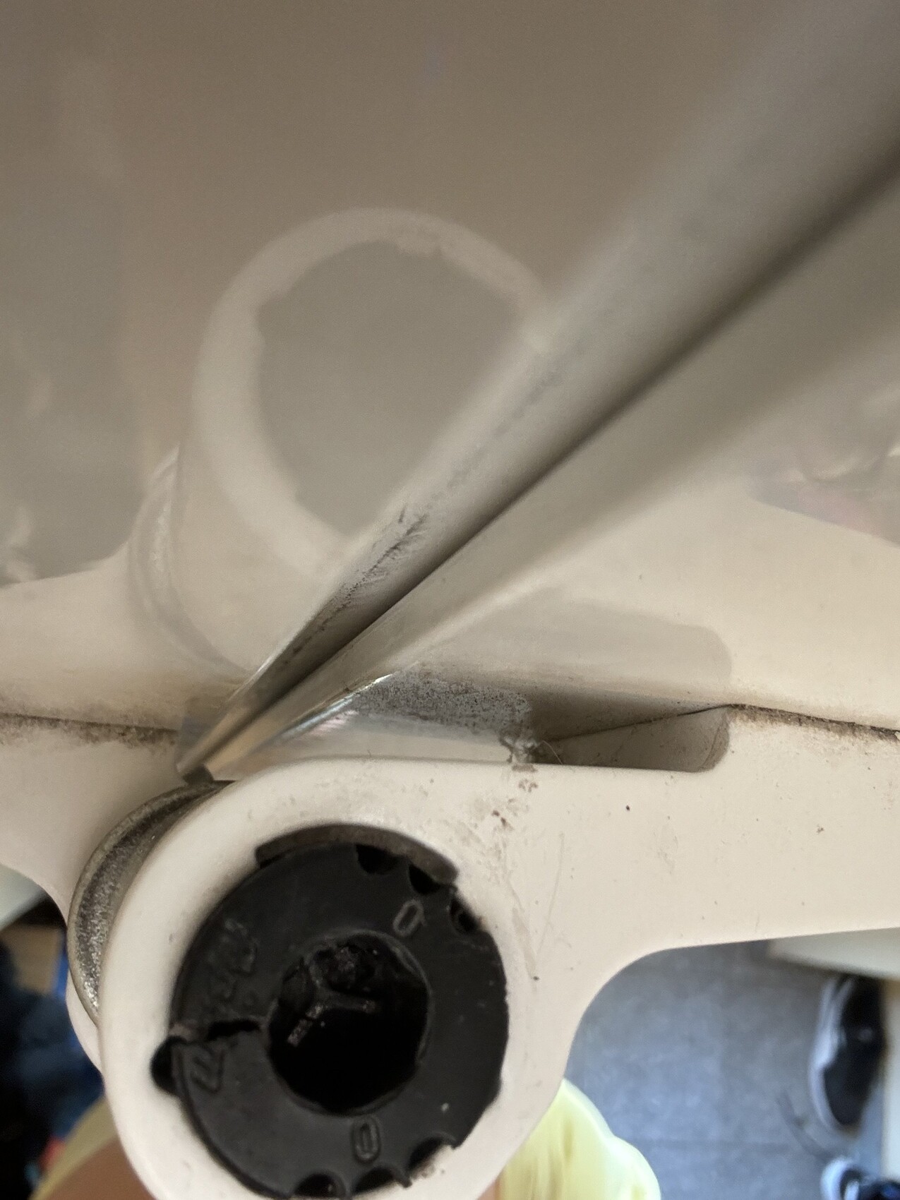 Nahaufnahme eines schwarzen Einstellknopfs an einem weißen Metall-Gelenk, Staubrückstände sichtbar.