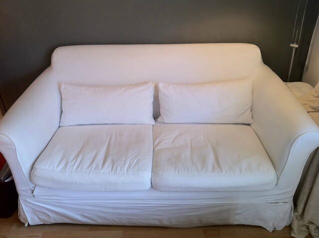 Weisses Sofa im Wohnzimmer mit zwei Kissen vor dunkler Wand
