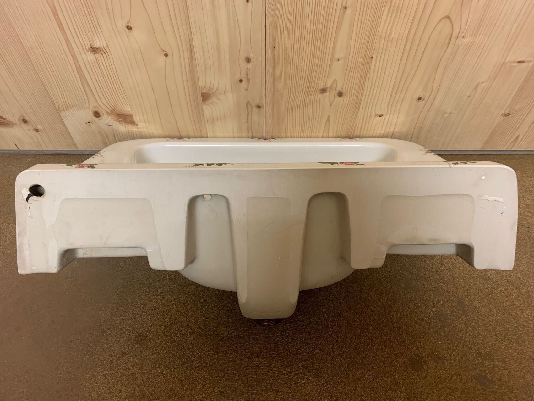 Weißer Sanitär-Unterbau mit Innenwanne, liegt flach auf dem Boden vor Holzwand.