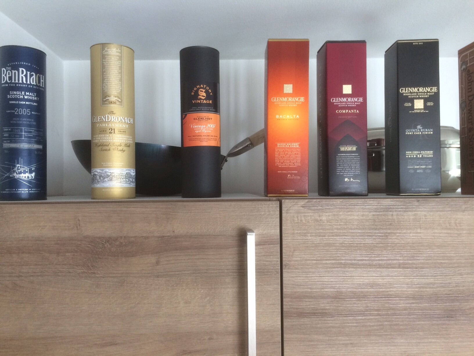 Verschiedene Whisky-Verpackungen stehen in Reihe auf einem Holzschrank.