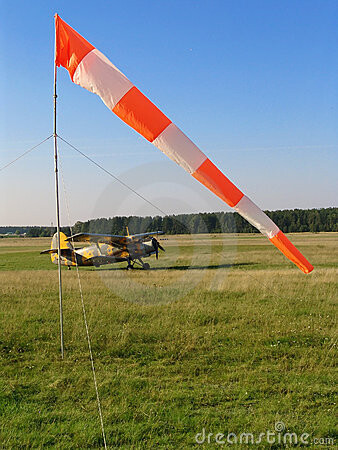 Windsack am Flugfeld mit kleinem gelben Flugzeug auf Grasbahn