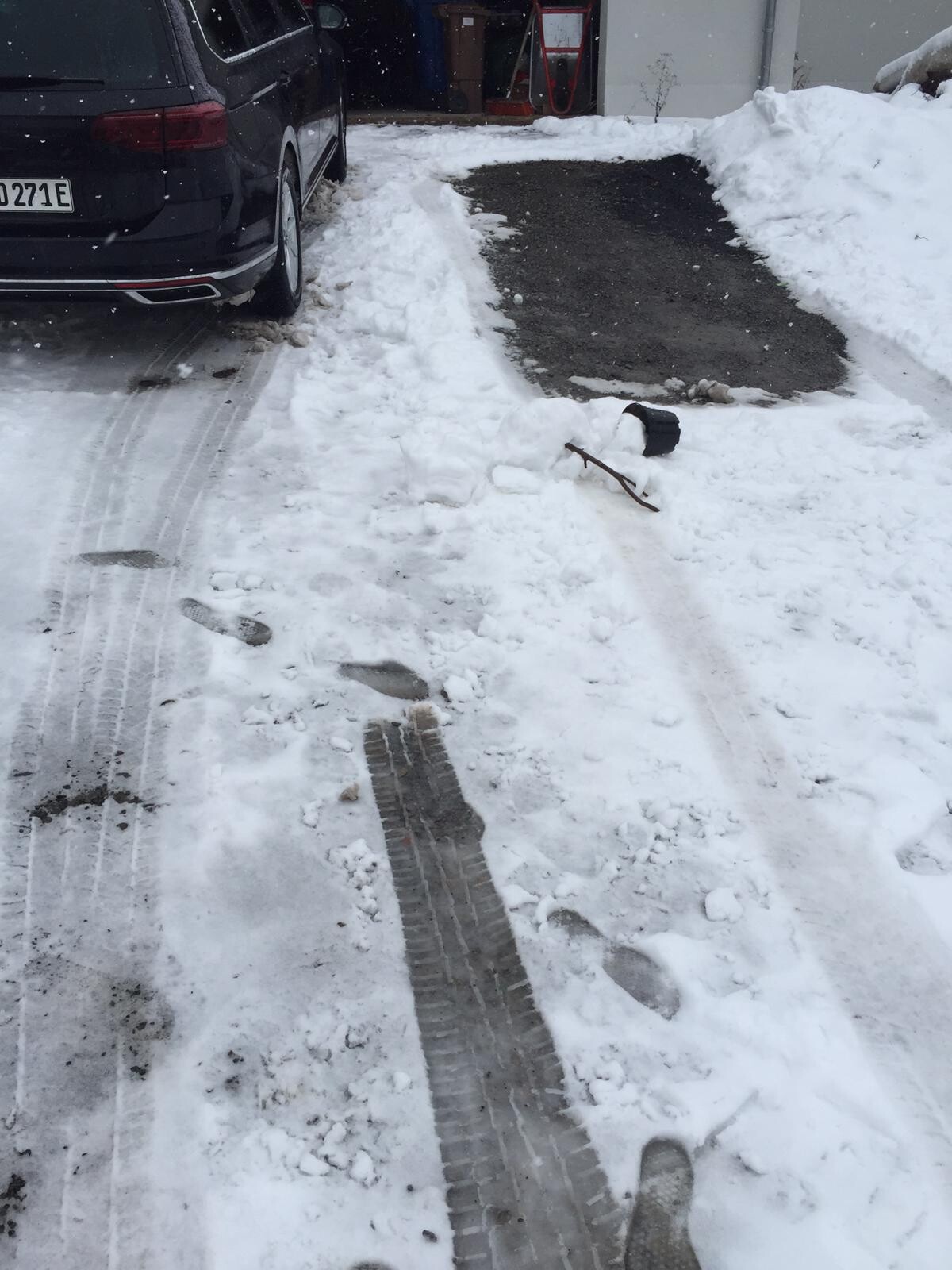 Schneebedeckte Einfahrt mit schwarzem Van, freigelegter Asphaltabschnitt und Werkzeug im Schnee.