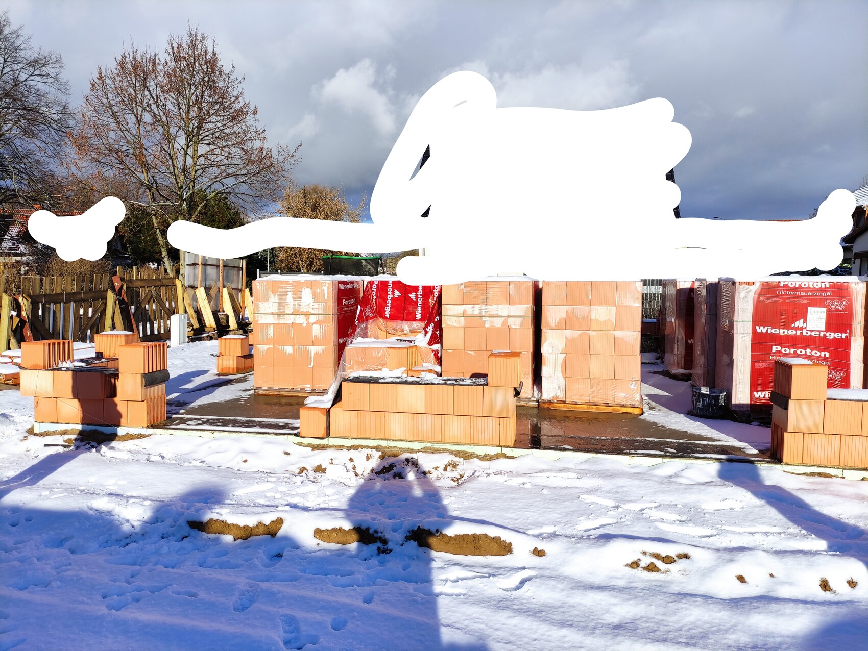Baustelle mit Ziegelsteinen auf Fundamentboden im Winter, Paletten und Schnee