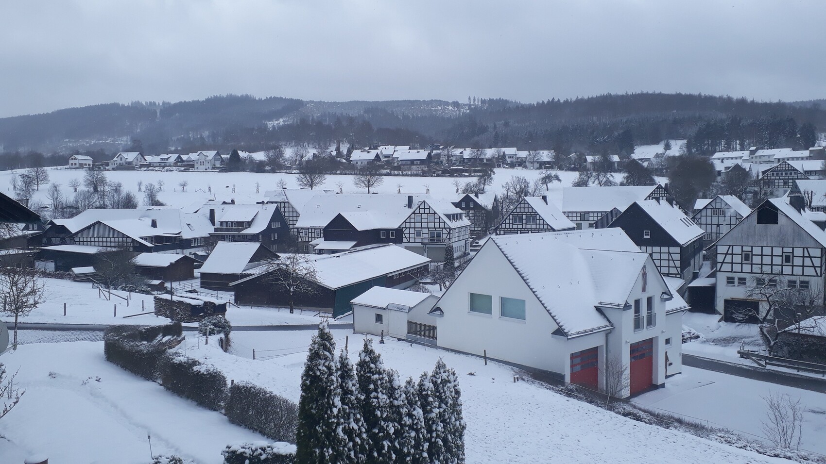 Winterliches Dorf mit schneebedeckten Fachwerkhäusern und einem weißen Haus mit roten Garagen.