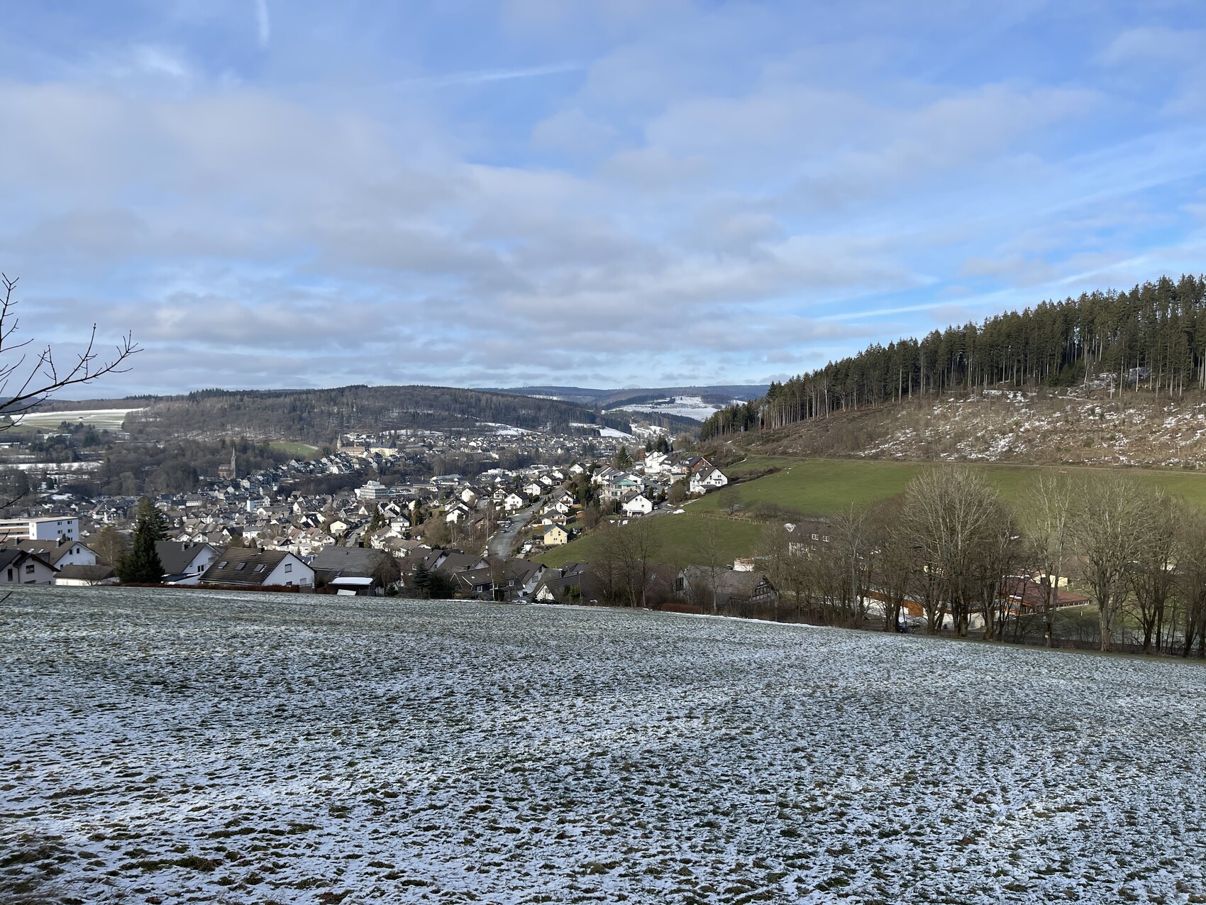 Kleines Dorf im Wintertal: Häuser am Talboden, rechter Hang mit Wald, Schnee bedeckt Felder.