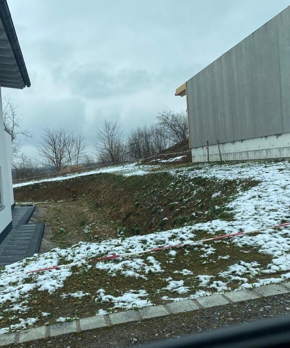 Außenansicht: verschneite Böschung zwischen Gebäuden; rotes Absperrband im Vordergrund.