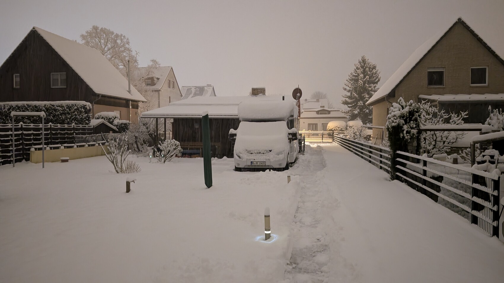 Verschneite Vorstadtstraße mit Schnee bedecktem Auto, Häusern und Zäunen.