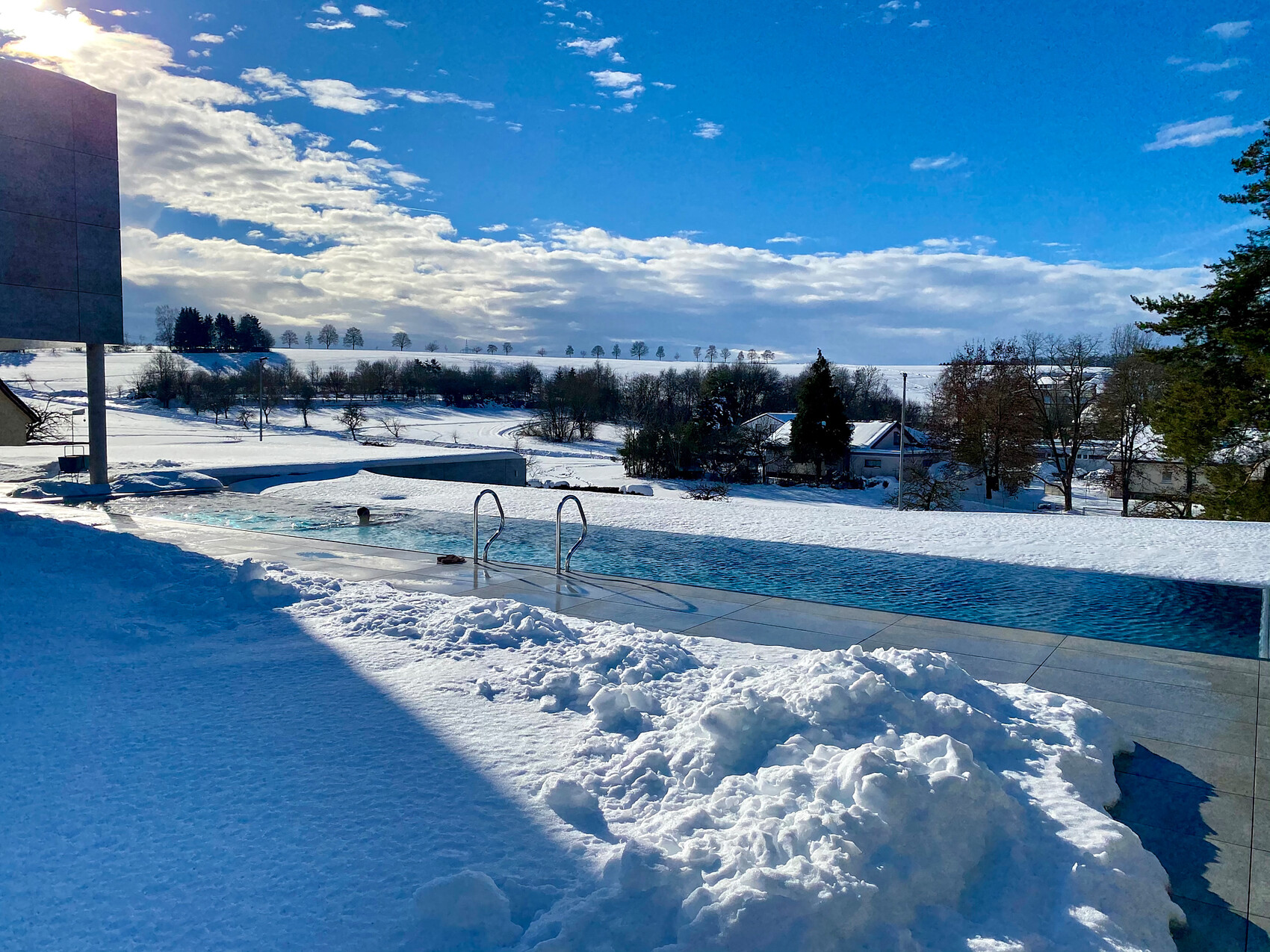 Außenpool im Schnee neben moderner Fassade und Winterlandschaft