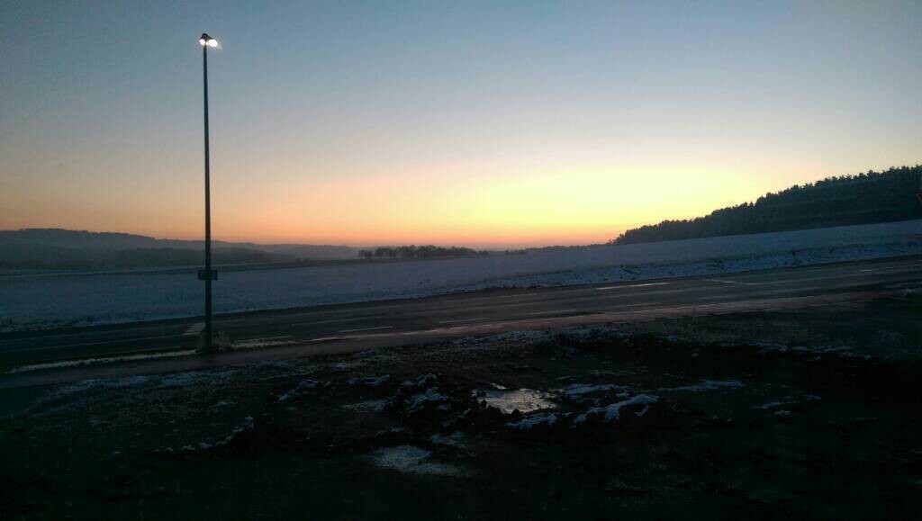 Sonnenuntergang über verschneiter Landschaft, eine Straßenlampe am Straßenrand.