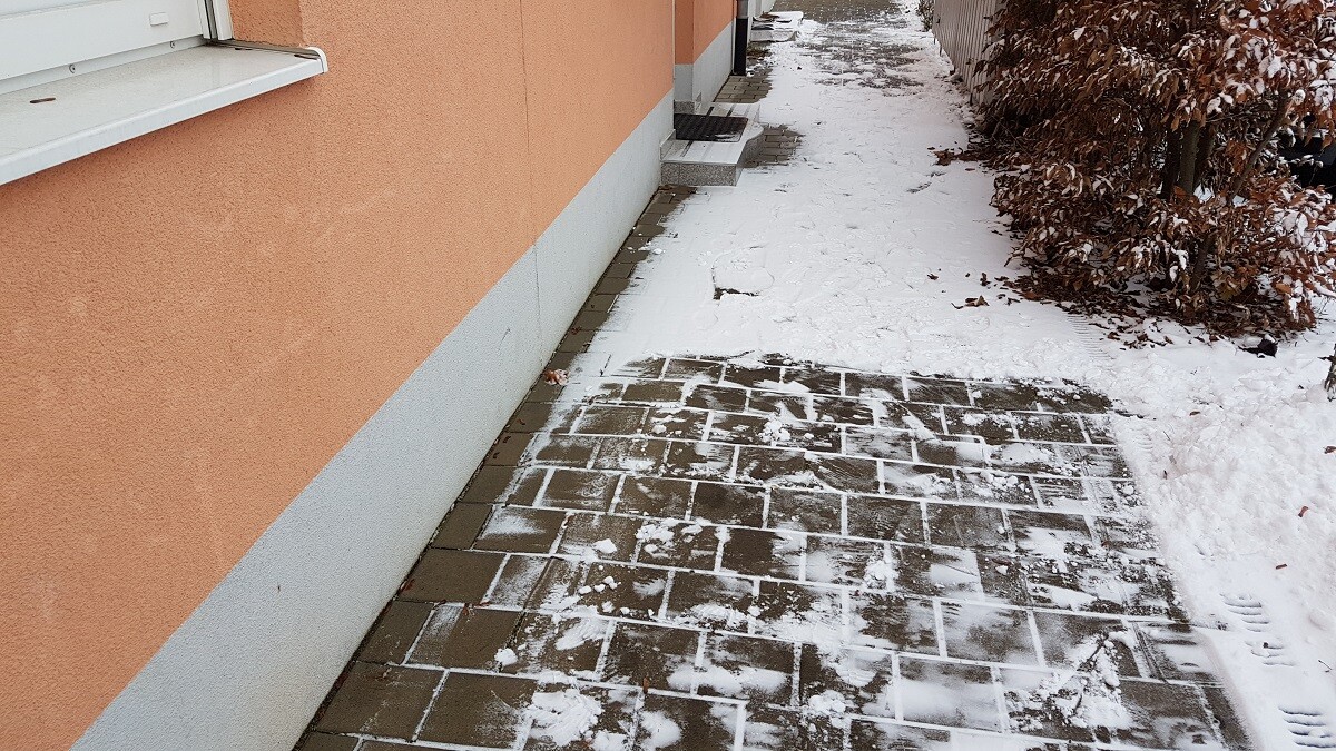 Verschneiter Terrassen-Vorplatz neben orangefarbener Hausfassade mit Pflastersteinen