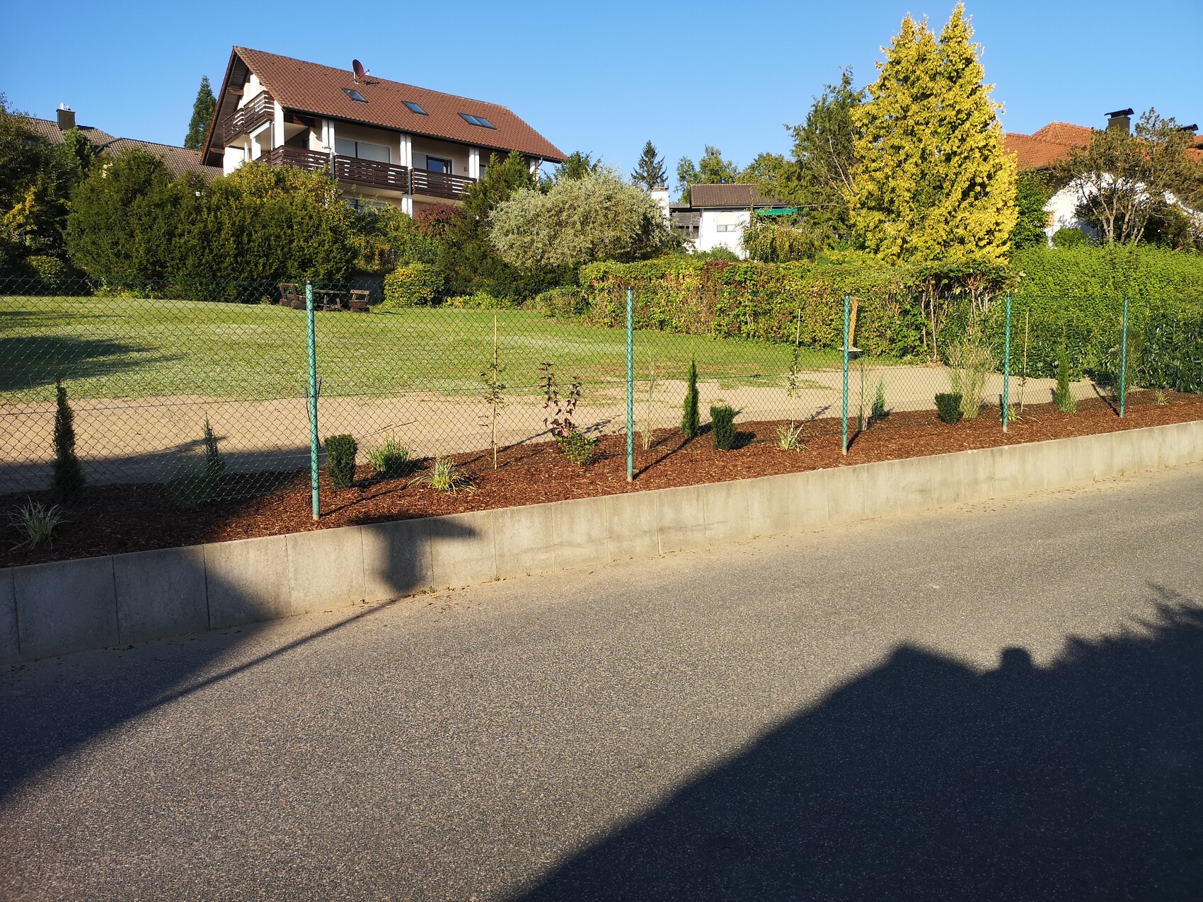 Wohnhaus mit rotem Ziegeldach, Garten, Hecken und Drahtzaun am Straßenrand