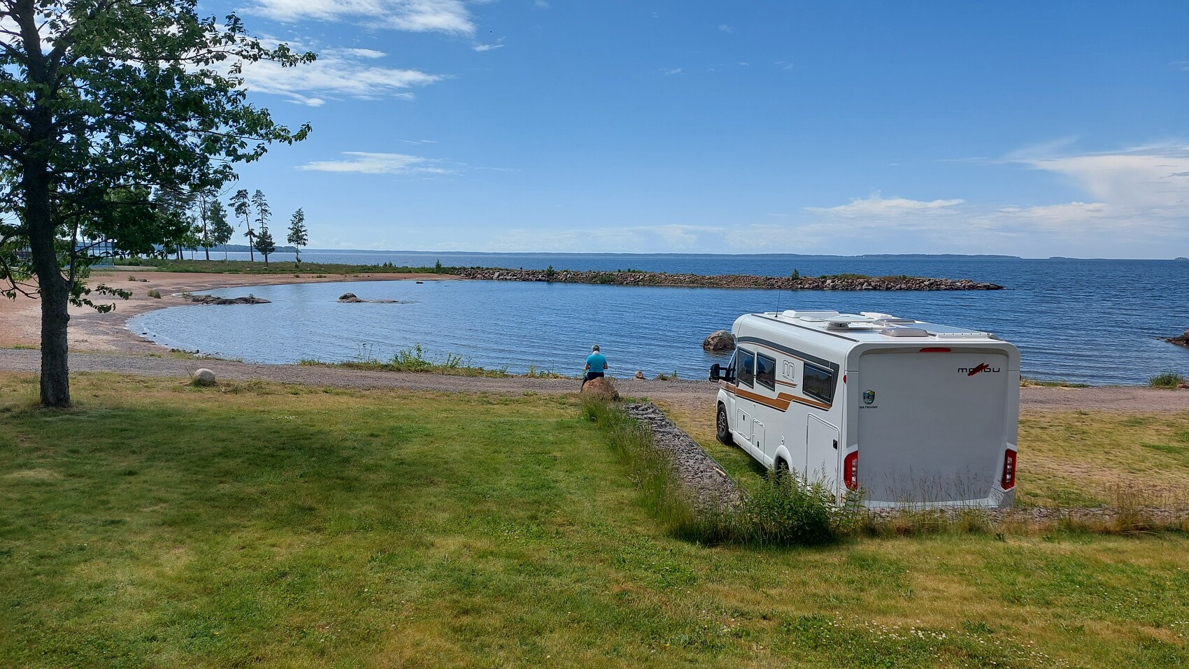 Wohnmobil am Seeufer; Angler am Ufer, ruhige Strandlandschaft mit Bäumen und See im Hintergrund