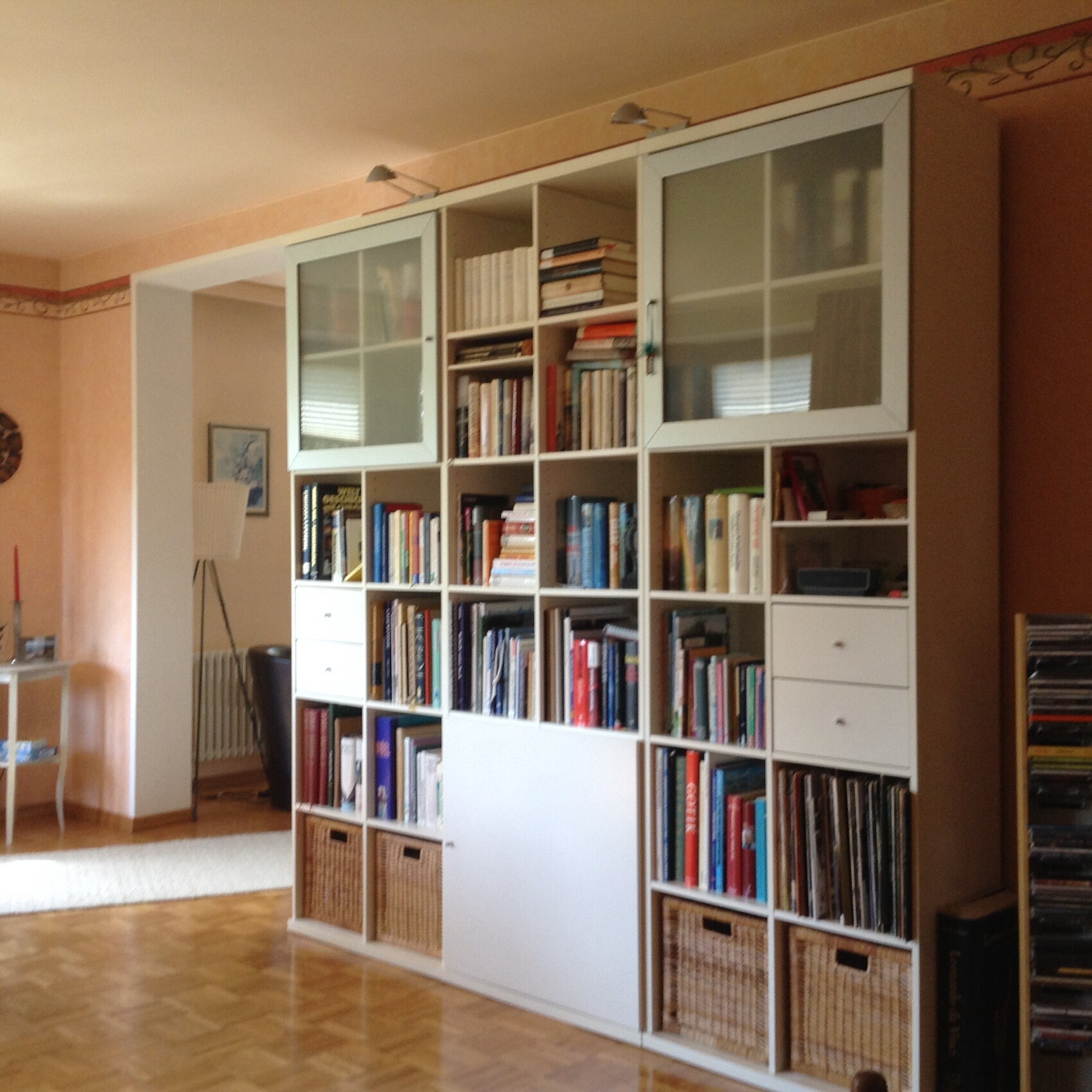 Großes weißes, modulares Bücherregal im Wohnzimmer mit vielen Büchern und Körben