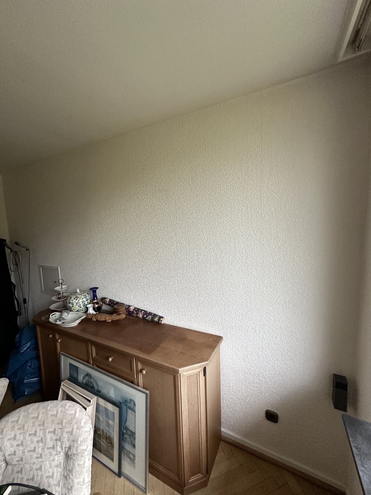 Holzkommode mit Geschirr, Vase und gerahmten Bildern in einer Dachboden-Ecke.