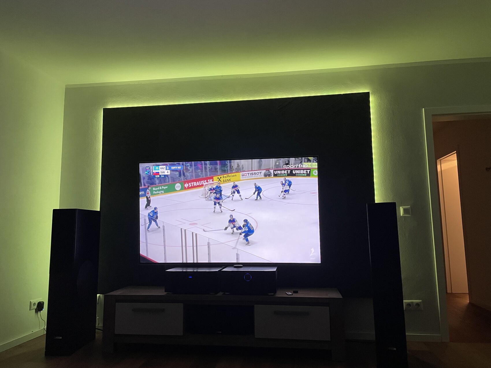 Flachbildfernseher zeigt Eishockeyspiel, grüne Ambientebeleuchtung im Hintergrund.