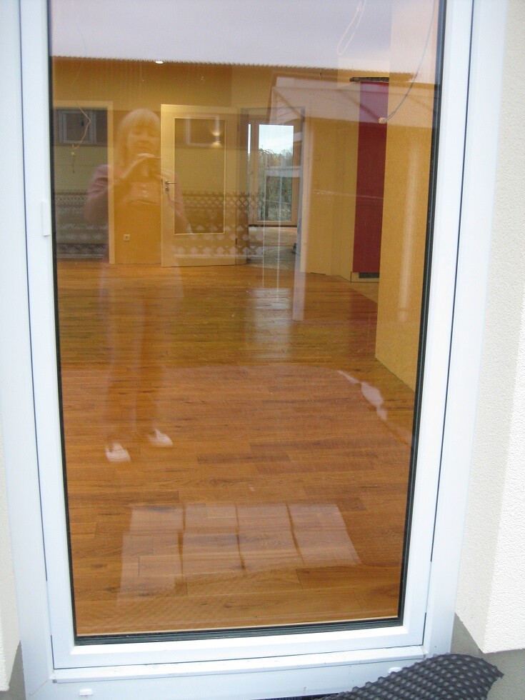 Wohnzimmer mit Holzboden hinter Glasfront, Reflexion einer Person beim Fotografieren.