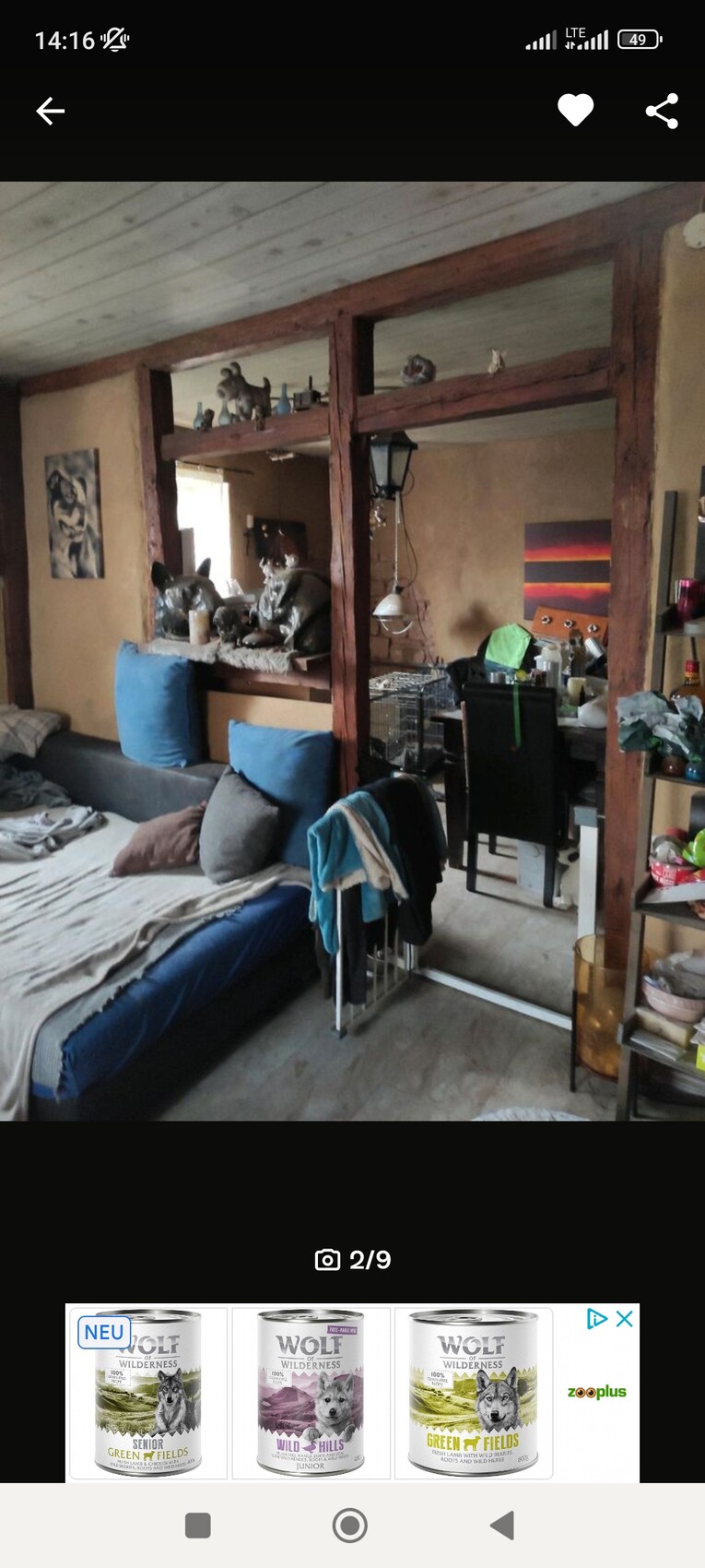 Wohnzimmer mit halboffener Holzwand-Trennwand, Sofa mit blauen Kissen und Deko-Figuren