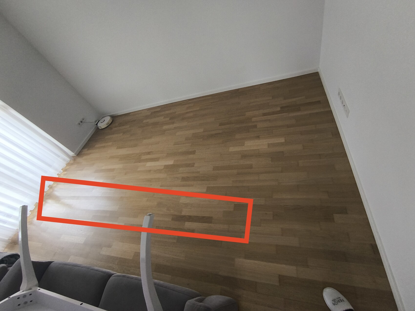 Wohnzimmer mit hellem Holzboden, weißen Wänden und roter Markierung auf dem Boden