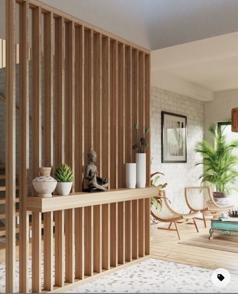 Wohnzimmer mit Holz-Trennwand, Konsole, Buddha-Statue, Vasen, Pflanze und Rattan-Sessel.