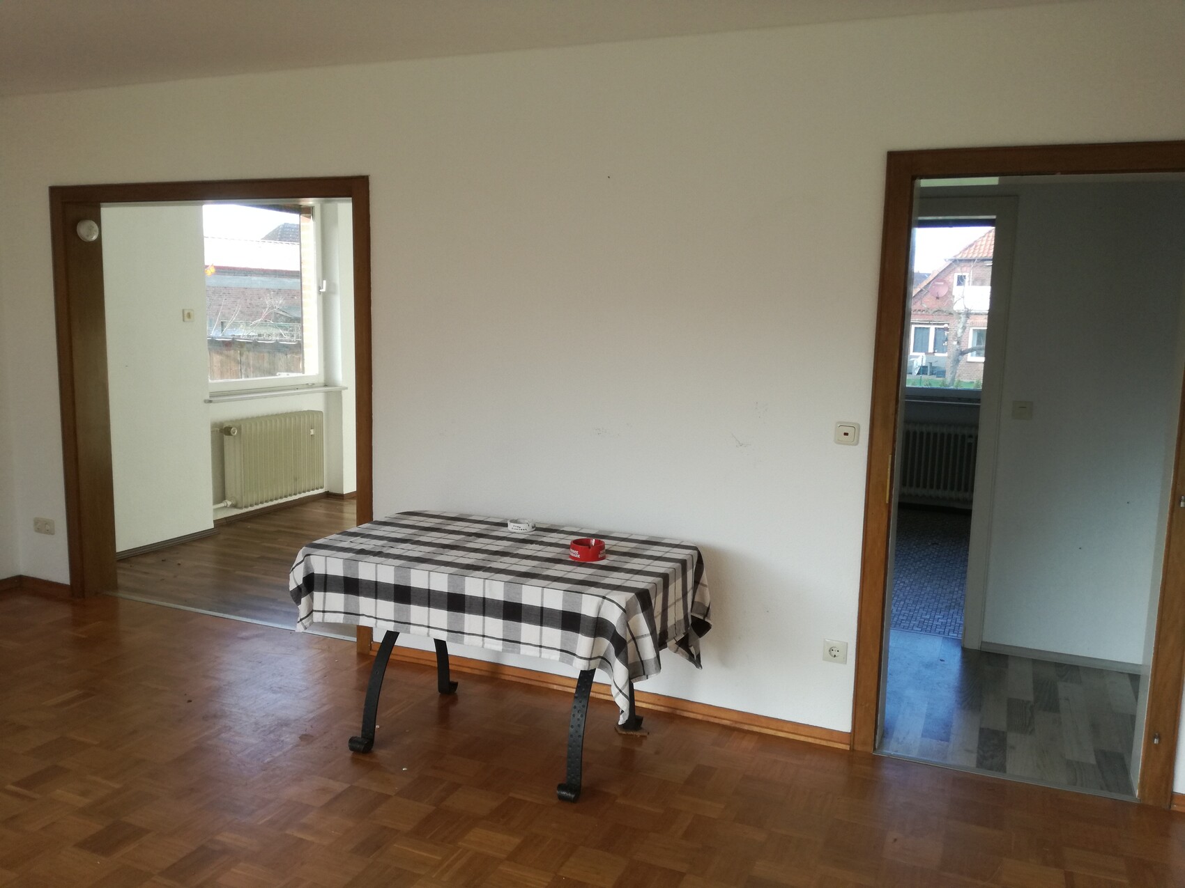 Helles Zimmer mit Holzboden, Tisch mit schwarz-weiß kariertem Tischtuch, zwei Türöffnungen.