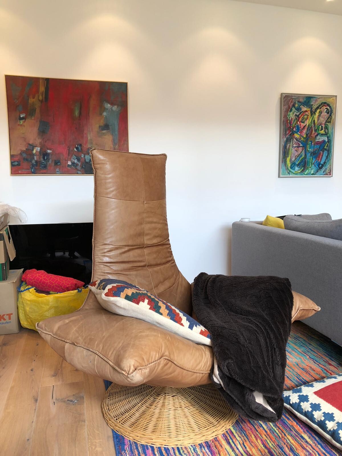 Modernes Wohnzimmer mit braunem Lederstuhl, bunten Kissen, farbigem Teppich und abstrakten Gemälden.