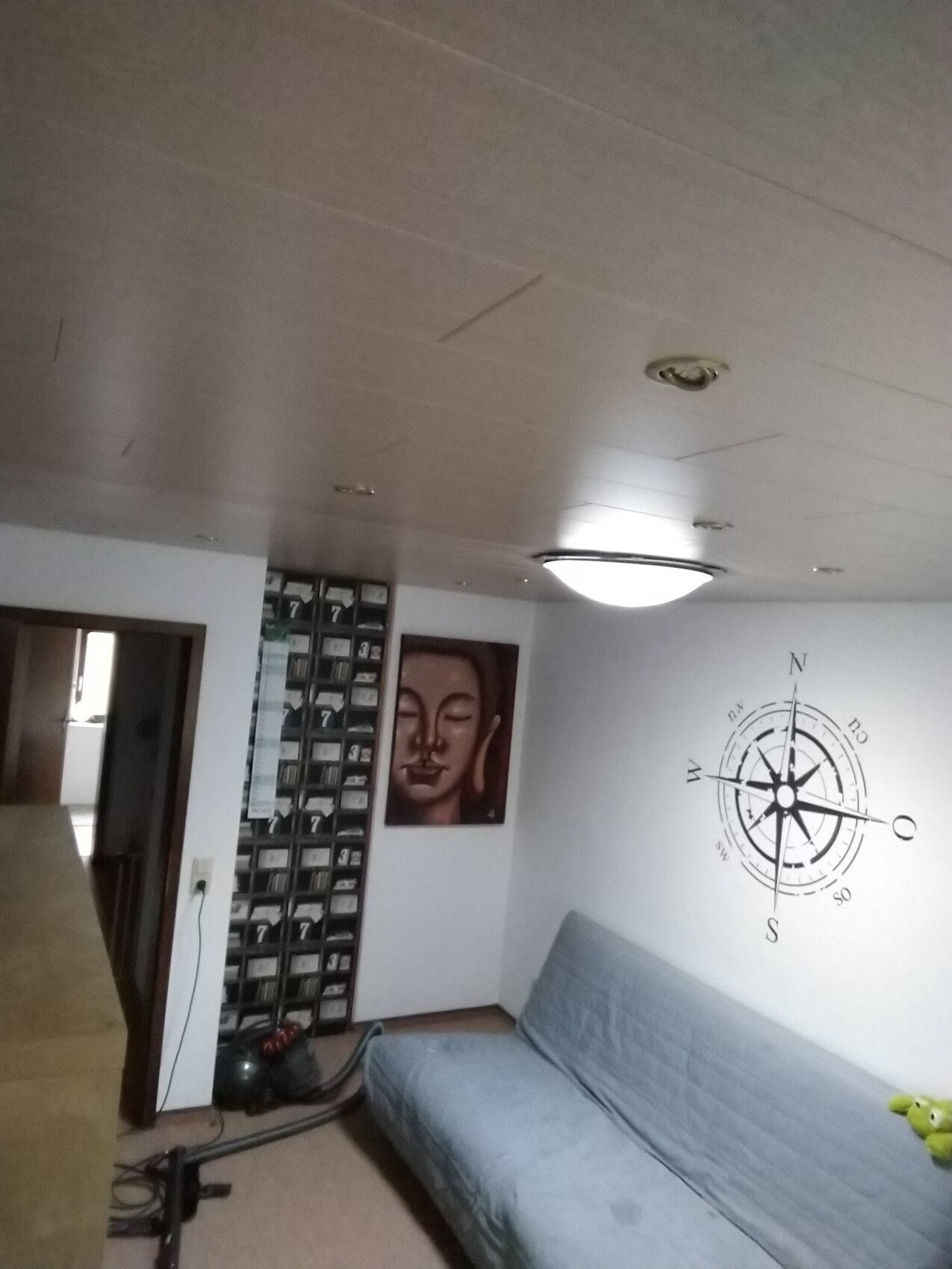 Kleines Keller-Wohnzimmer mit grauem Sofa, Kompass-Wandgrafik und Buddha-Bild