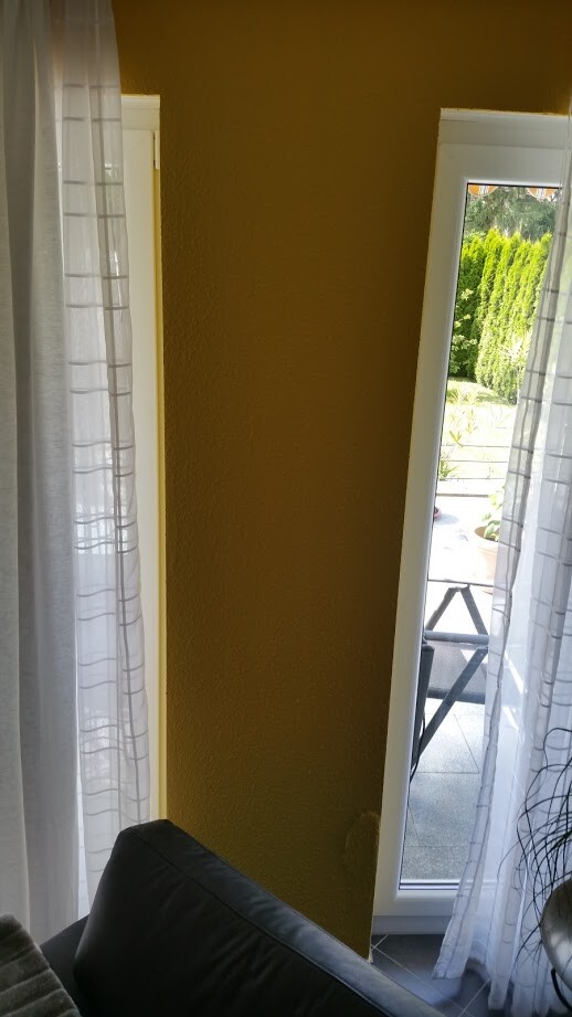 Wohnzimmer mit gelber Wand, weißen Vorhängen und Balkonblick.