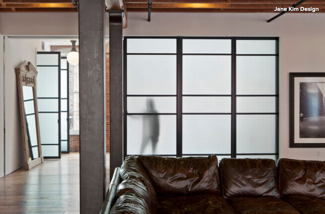 Wohnzimmer mit braunem Ledersofa und Milchglas-Glaswand mit Metallstützen.