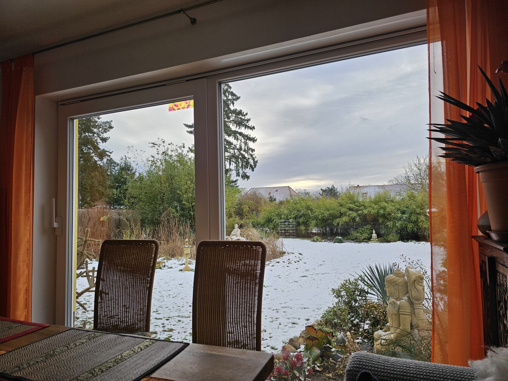 Esszimmer mit Esstisch, zwei Stühlen; offene Glasschiebetür zum verschneiten Garten mit Skulpturen.