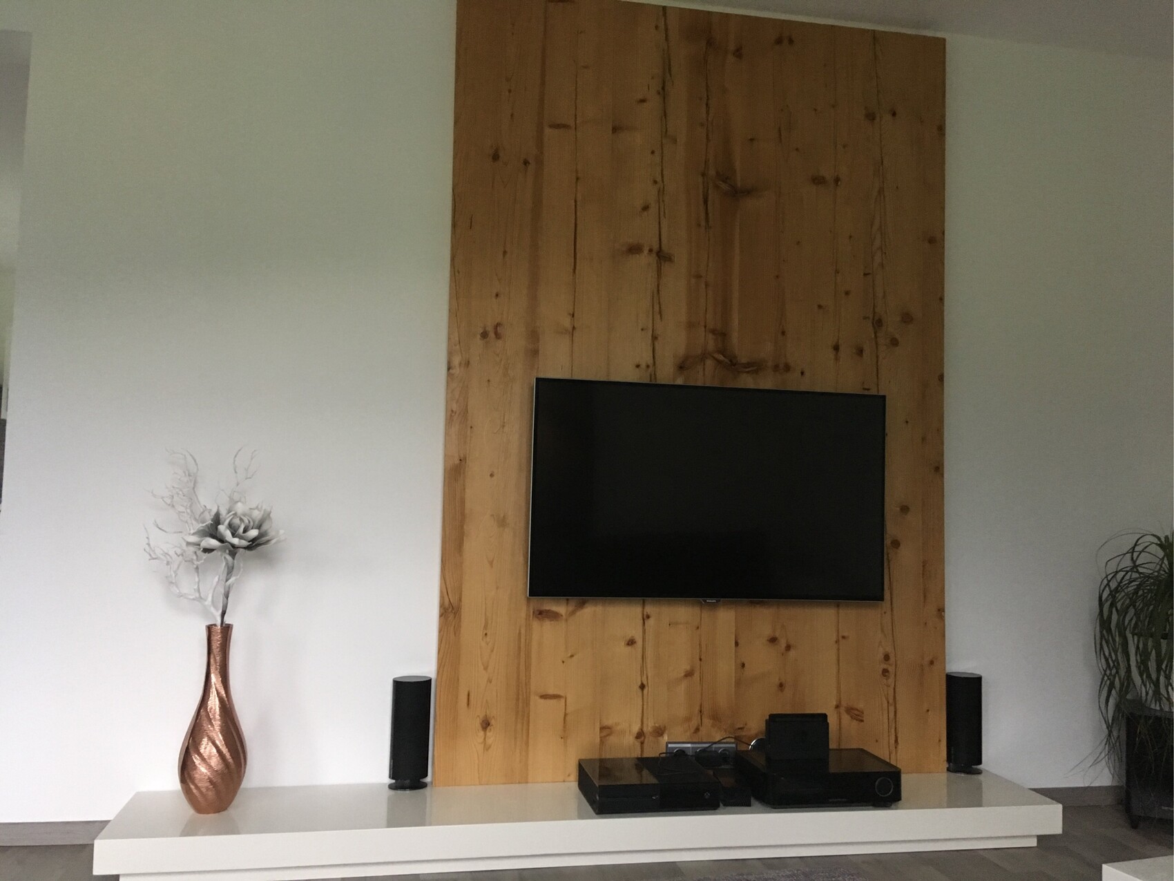 Wohnzimmer mit Holzpaneelwand, Flachbildfernseher und TV-Konsole.
